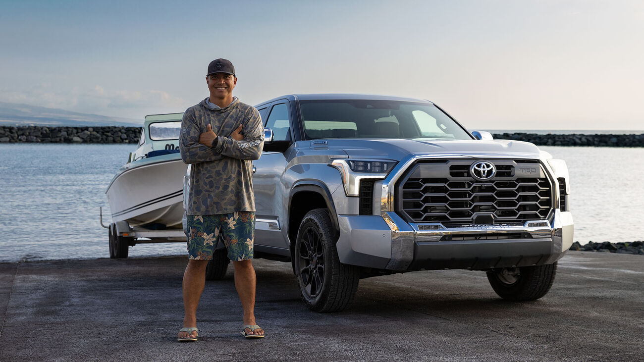 2026 Toyota Tundra i-FORCE MAX towing a small boat at the boat dock with the an athletic male posed next to the vehicle.