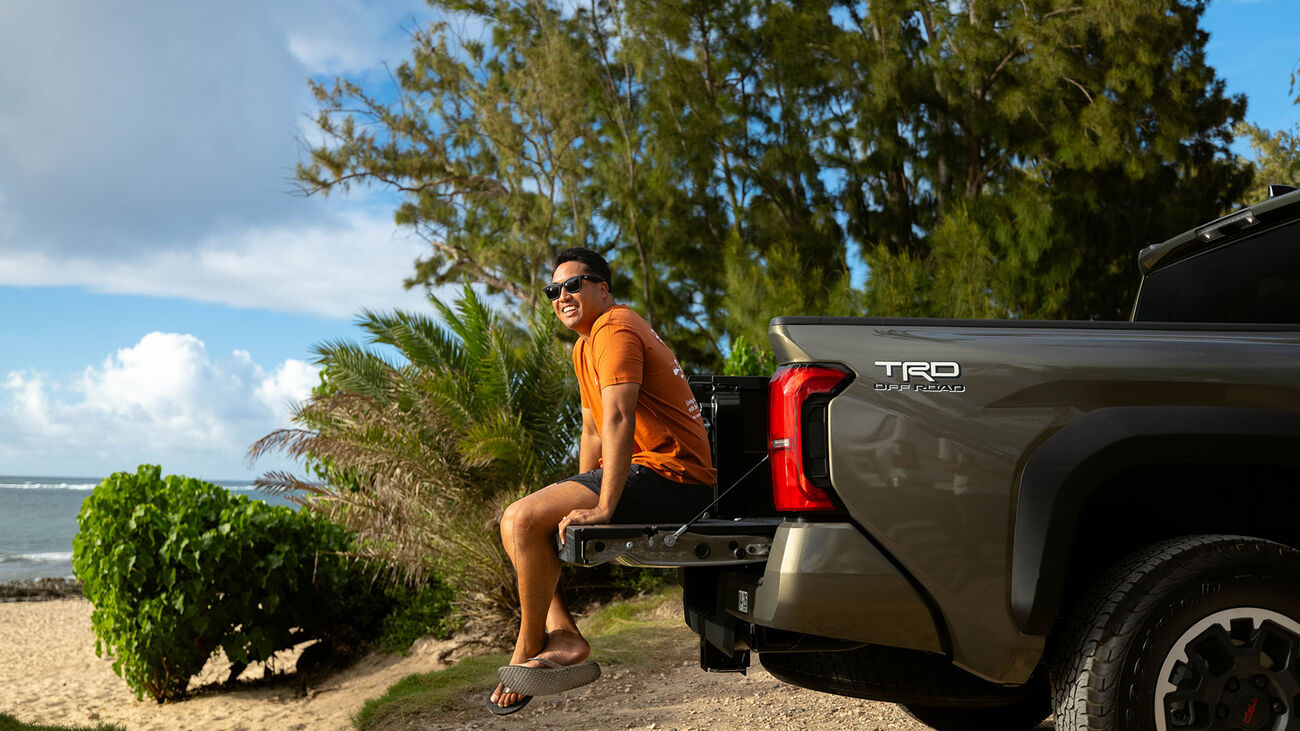 Toyota Hawaii ambassador Zavier Cummings posed seated in the bed of his 2026 Tacoma parked at the beach.