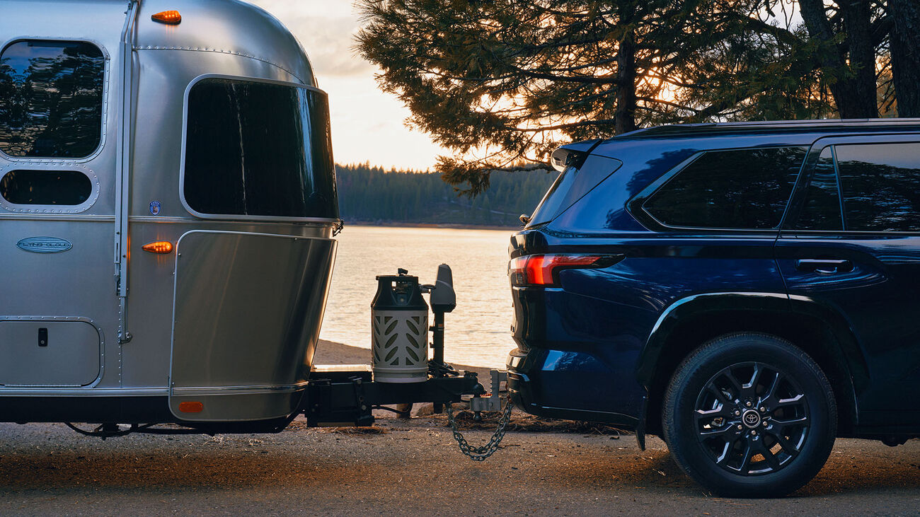 Toyota Sequoia Platinum in Blueprint parked in front of a lake with an airstream camper attached to the tow hook.