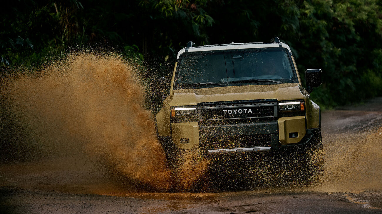 Toyota Land Cruiser in Trail Dust speeding through a mud puddle, splashing water as high as the vehicle.