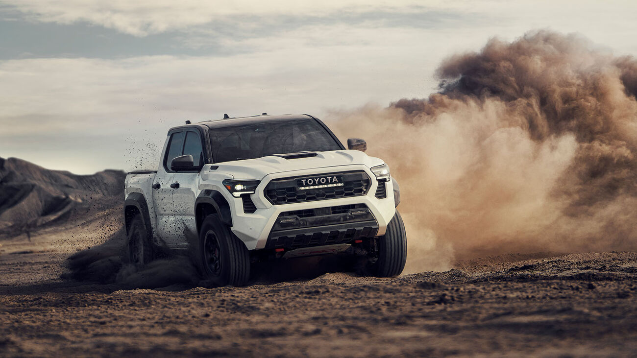 Toyota Tacoma i-FORCE MAX TRD Pro in Ice Cap with black roof performing donuts in an open desert with a cloud of smoke following.