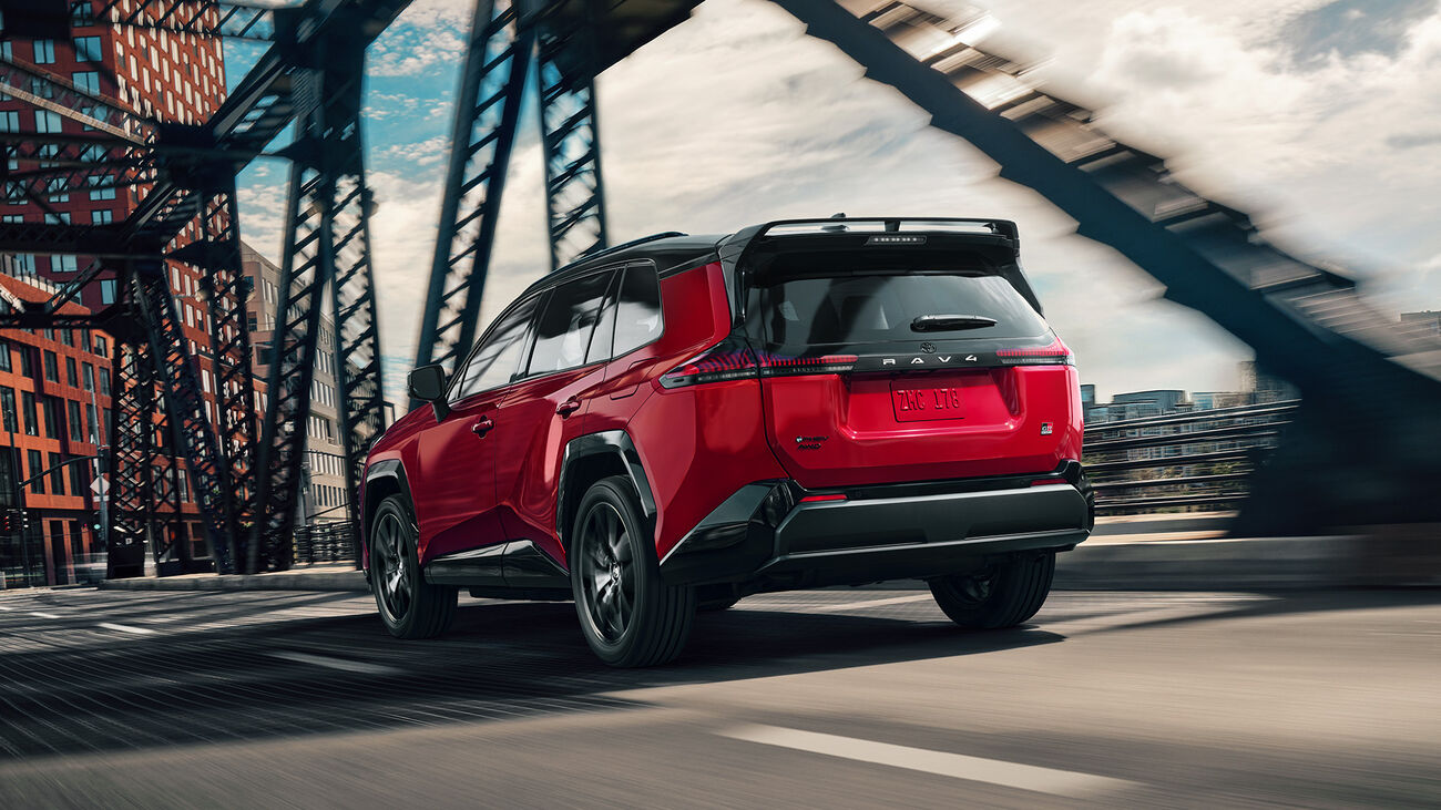 RAV4 Plug-in Hybrid GR Sport in Supersonic Red with Midnight Black Metallic roof driving away over a city bridge