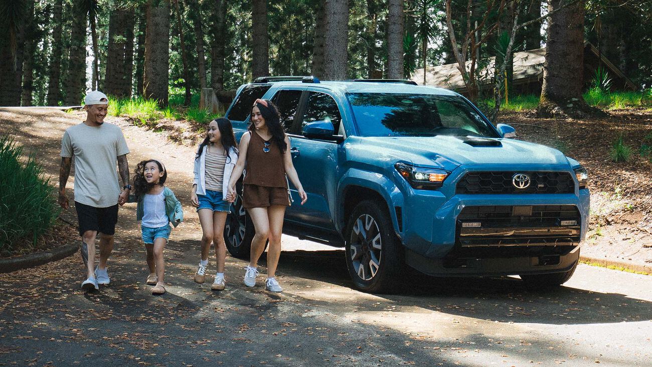 2026 Toyota 4Runner TRD Sport parked in a dense forest with a family of four walking past the vehicle.