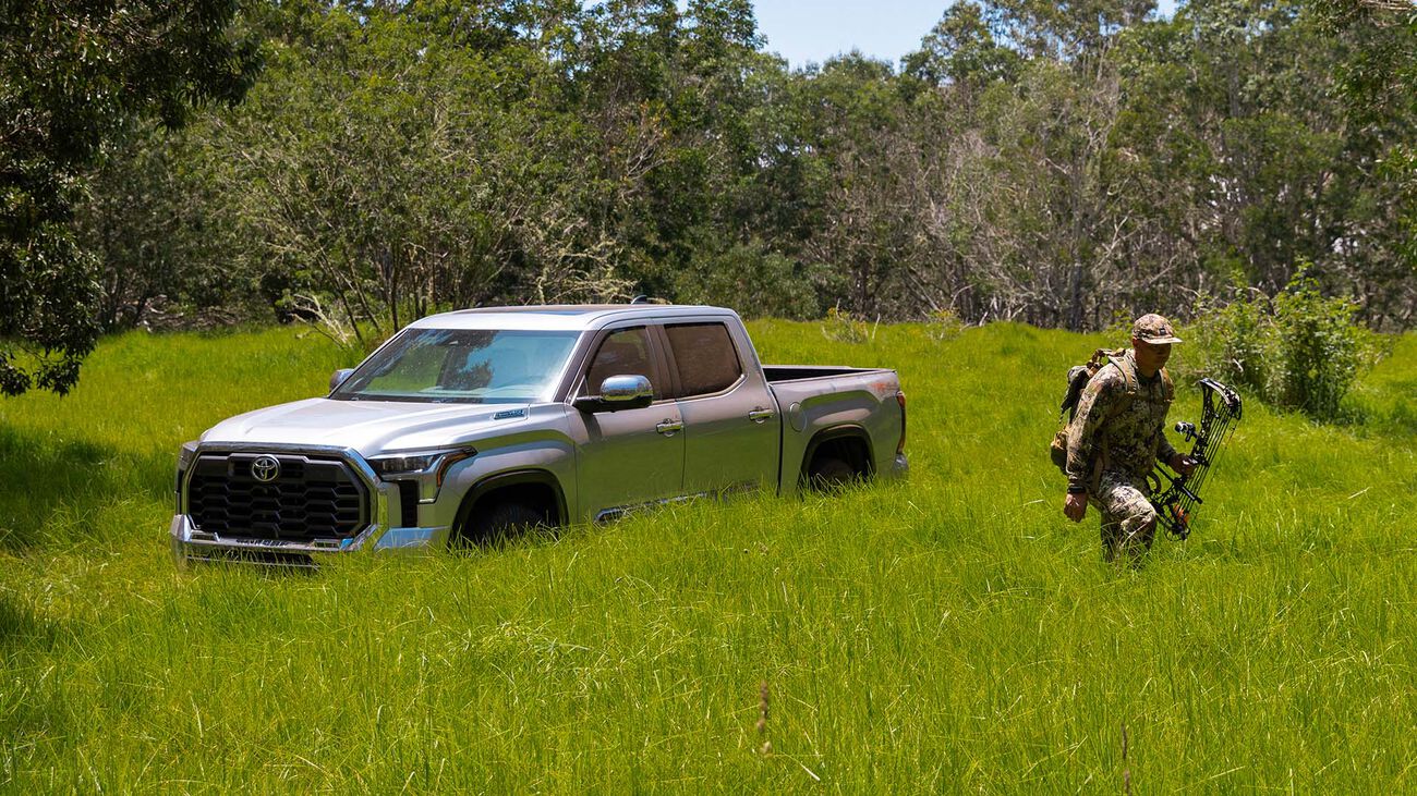 2026 Tundra i-FORCE MAX parked in a field of tall grass with the driver gearing up to go hunting.