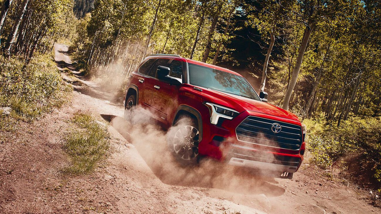 Toyota Sequoia Limited in Supersonic Red with power-extending tow mirrors speeding down a dirt road as a cloud of dust follows. 