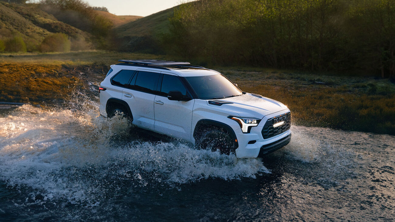 Toyota Sequoia TRD Pro in Ice Cap driving through a shallow river, splashing water a few feet high. 
