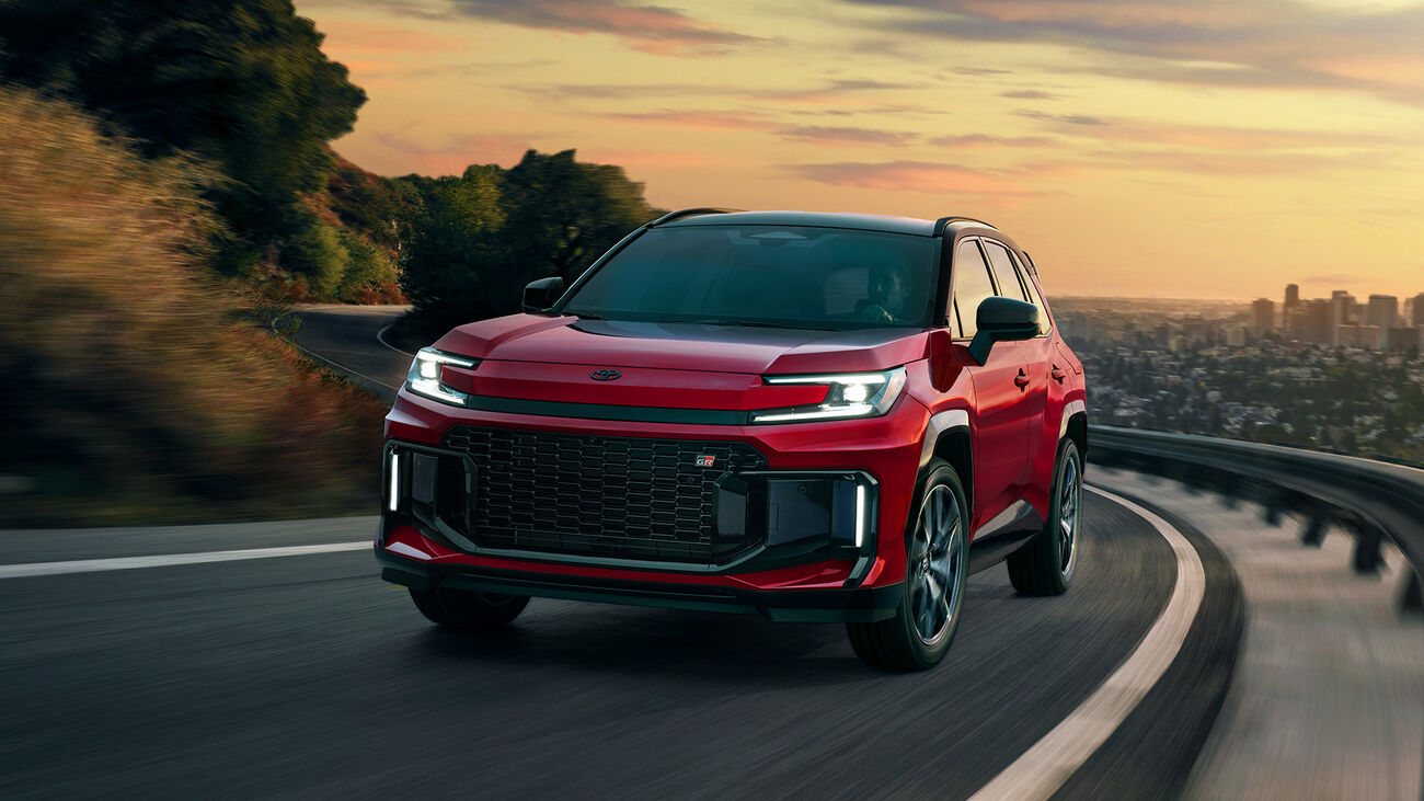 RAV4 Plug-in Hybrid GR Sport in Supersonic Red with Midnight Black Metallic roof driving on a curvy mountain road as the sun sets in the background.