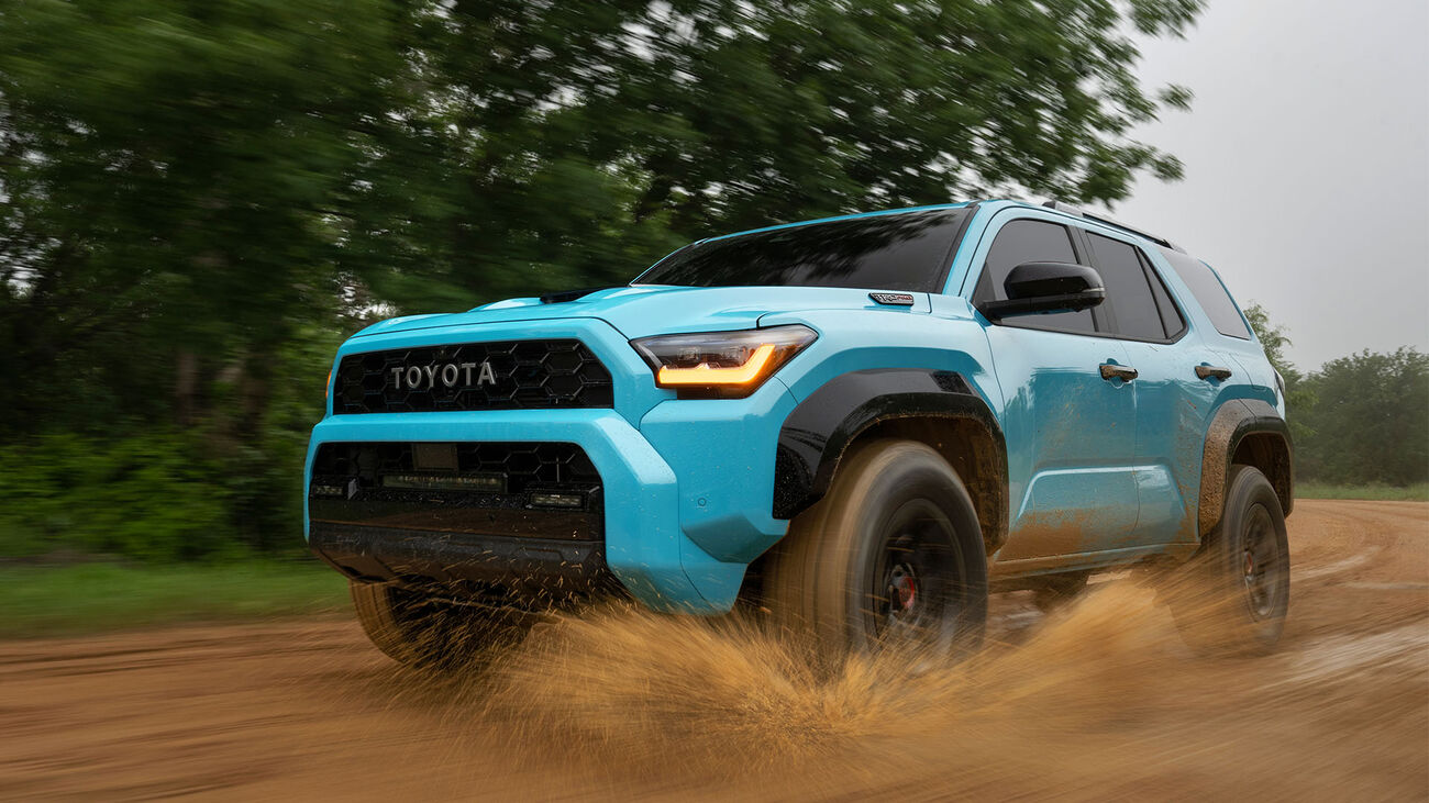 Toyota 4Runner i-FORCE MAX TRD Pro in Wave Maker driving through a muddy puddle in front of some greenery