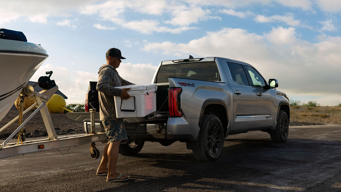 2026 Toyota Tundra i-FORCE MAX towing a small boat with the male driver loading a large cooler into the bed of the truck.