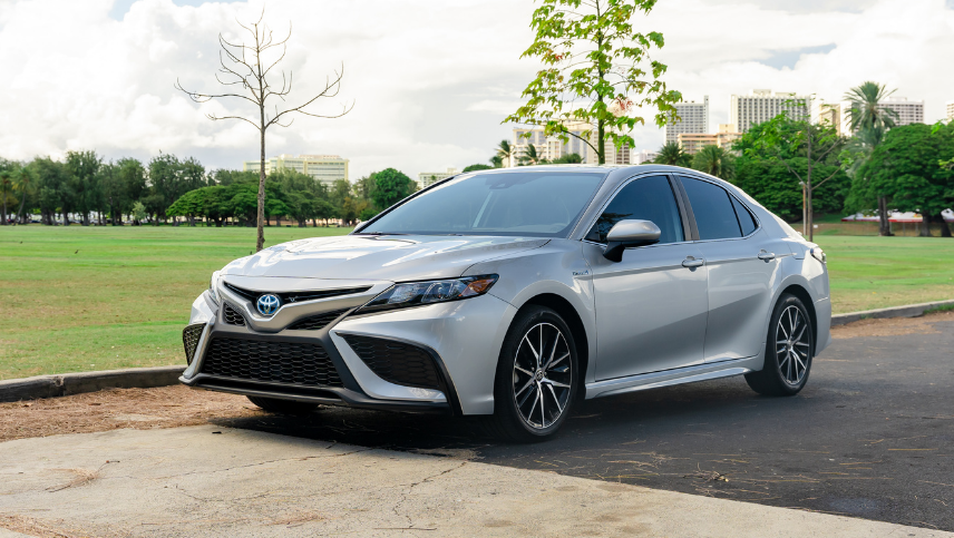 2022 CamryHybrid SE in Celestial Silver Metallic driving along park parking lot.