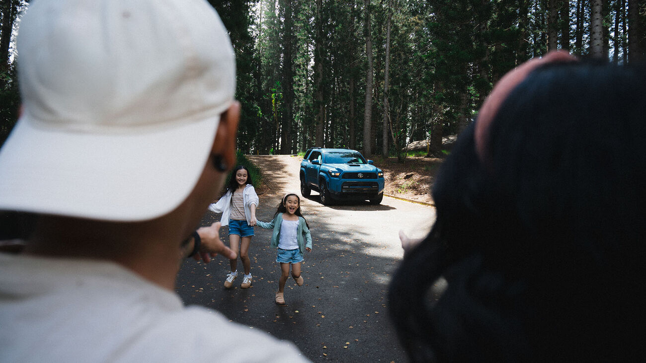 Over the shoulder view of the couple&rsquo;s two daughters playfully running towards them with the 2026 Toyota 4Runner TRD Sport in the background.